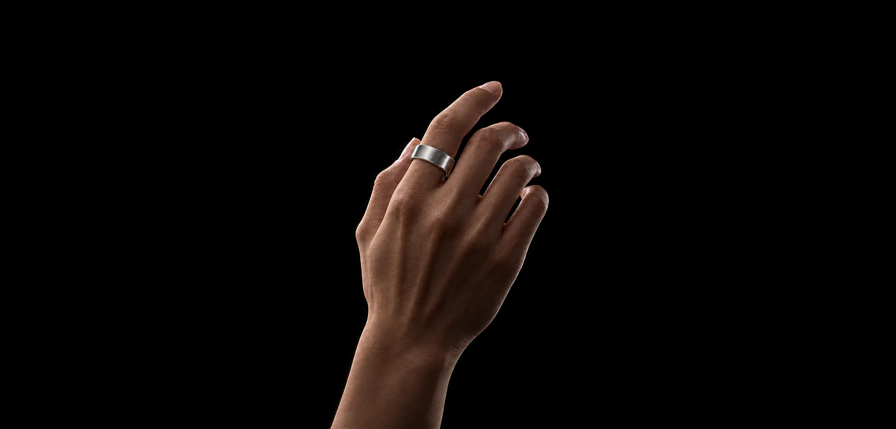 İşaret parmağında Brushed Silver PhenomeTech Ring takılı bir el; siyah zemin önünde aydınlatılmış, ön kol karanlığa karışıyor
