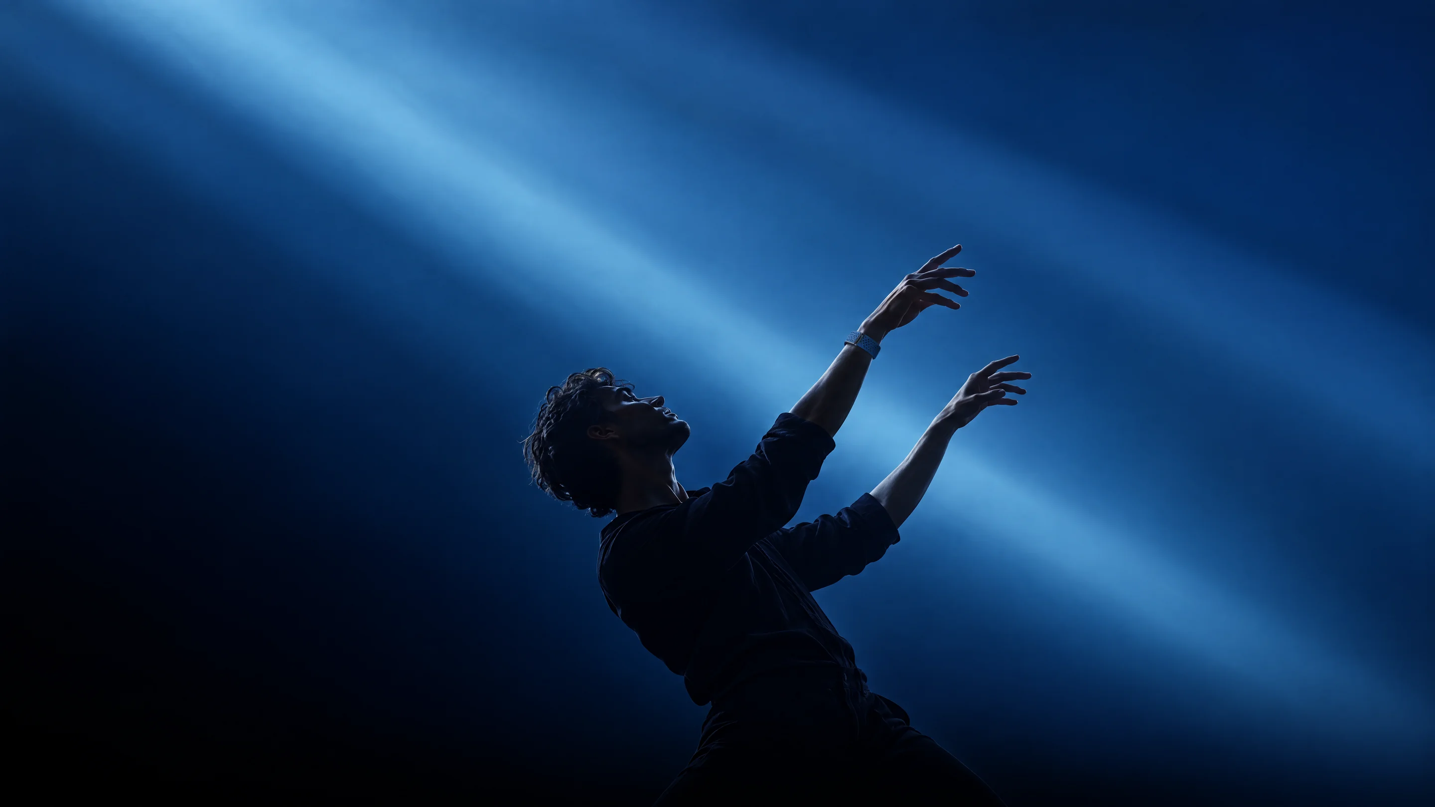 A man leaning back with both arms raised through beams of blue light, wearing the PhenomeTech Band in Harbour on the wrist