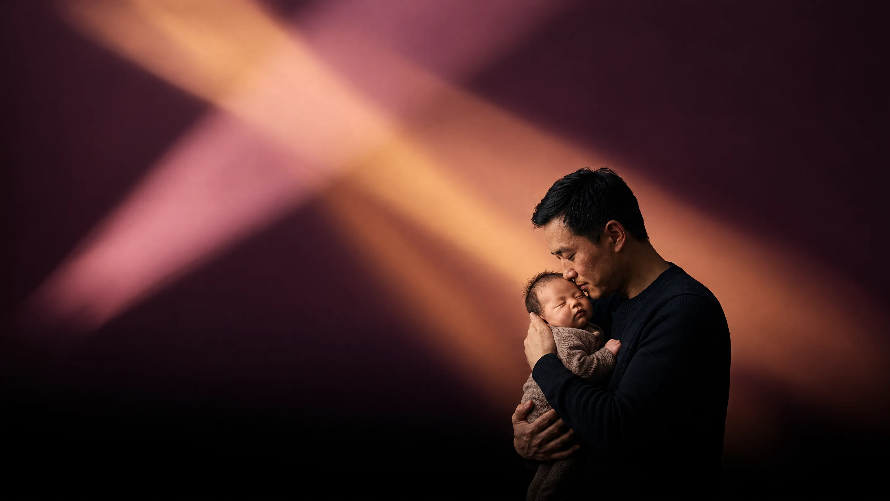 A father holding his sleeping newborn against his chest in beams of amber light