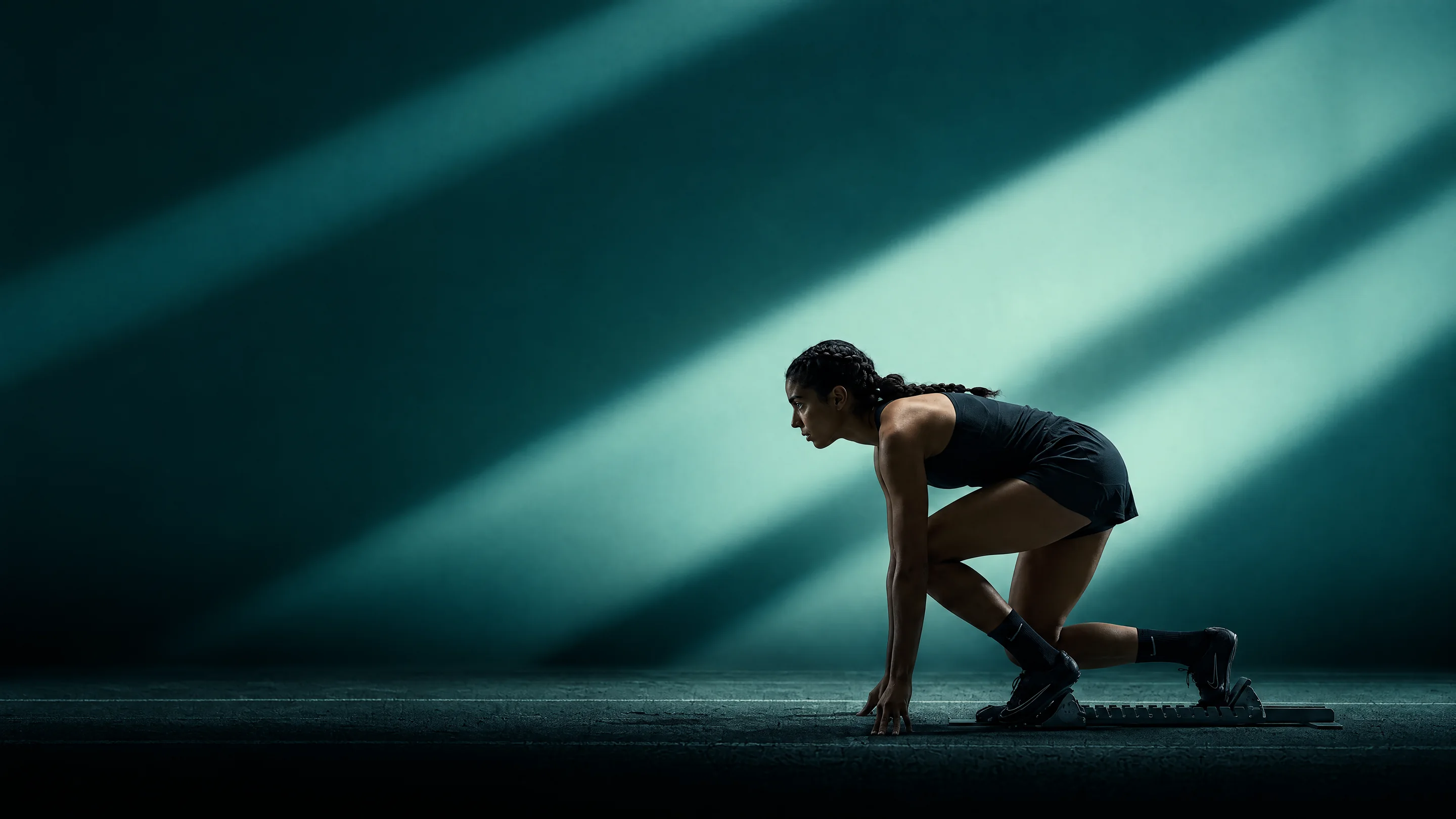 A sprinter crouched at the start in beams of teal light
