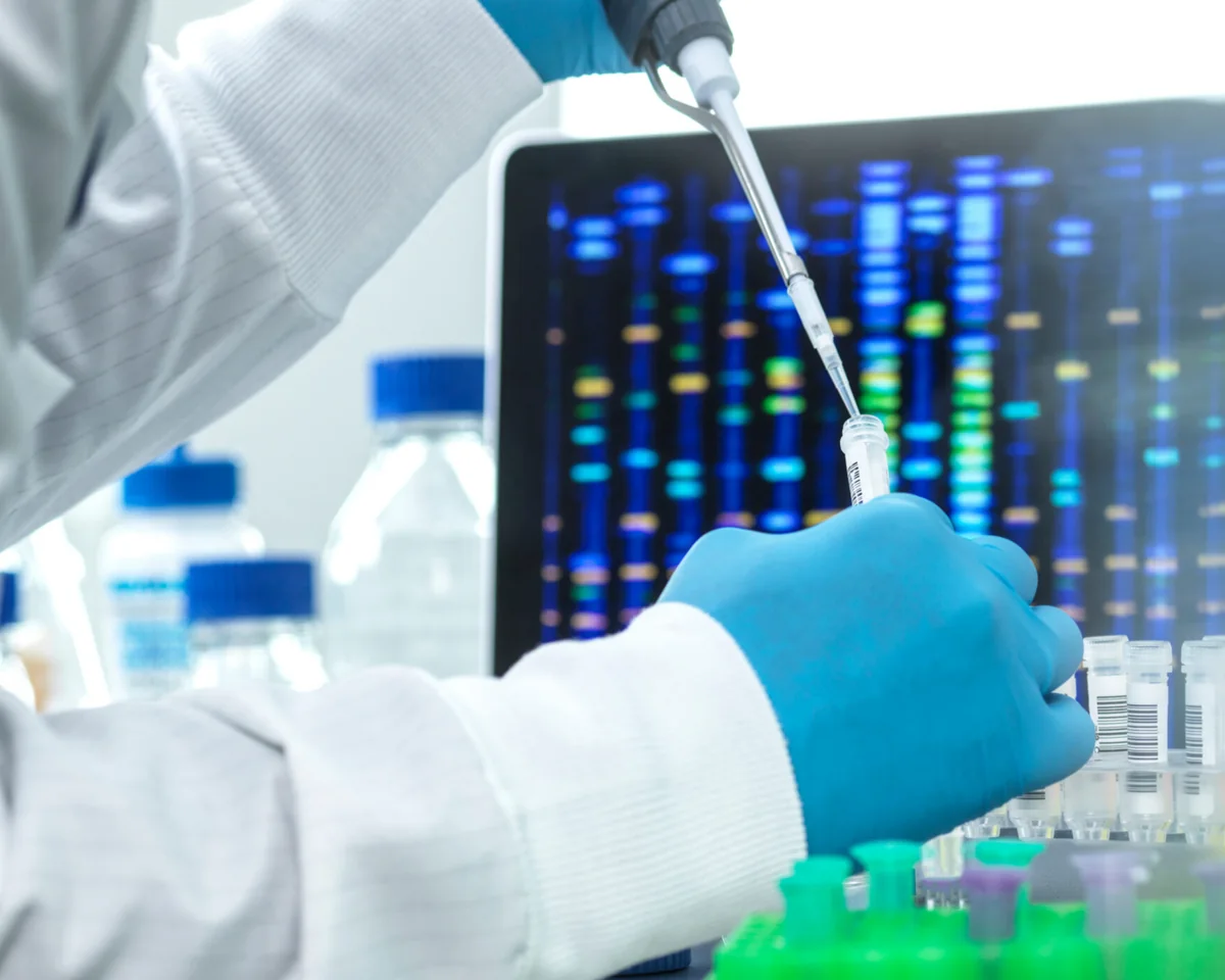 A scientist pipetting a sample in front of a sequencing read