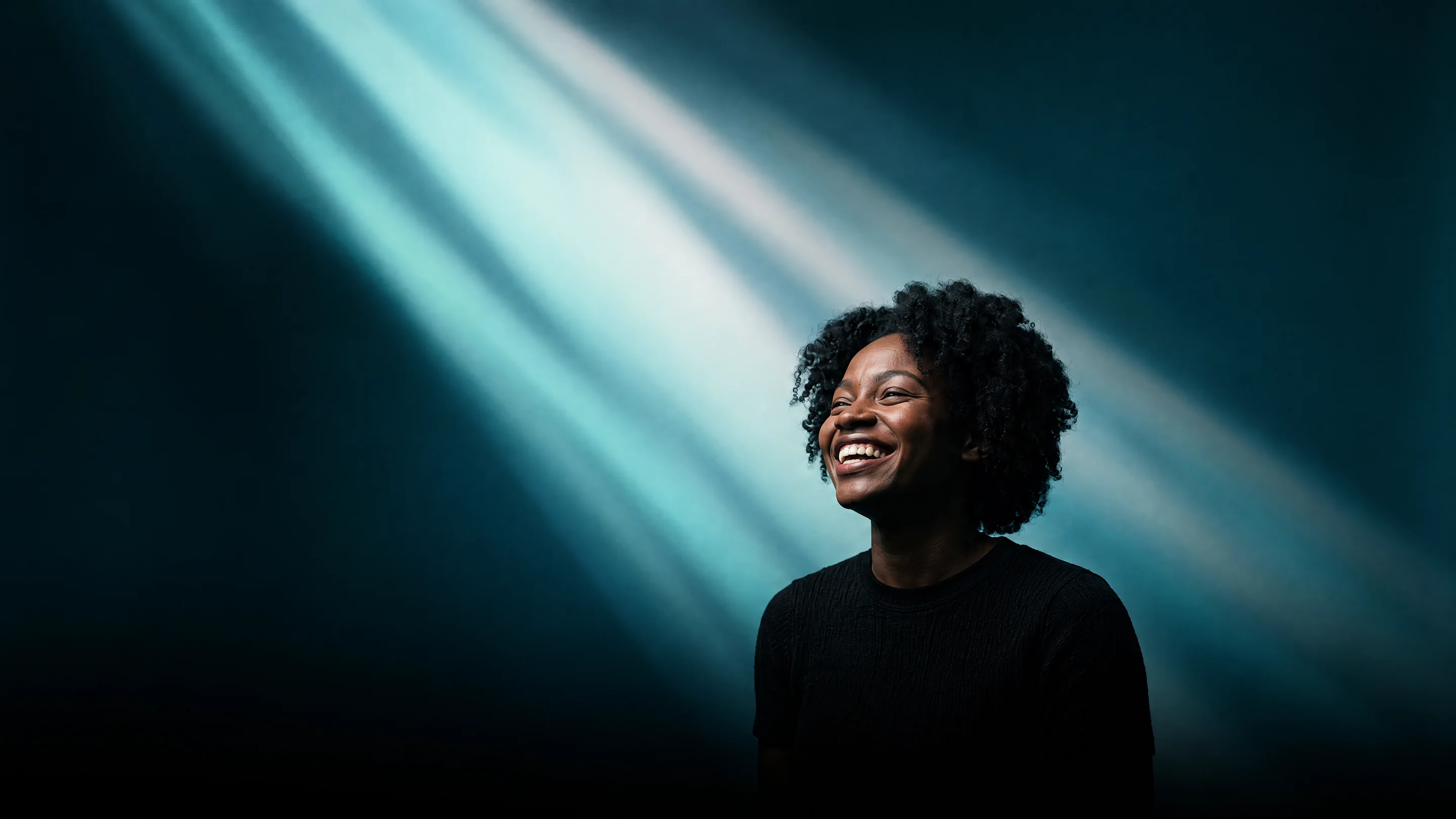 A young woman laughing with a wide open smile in beams of aqua light