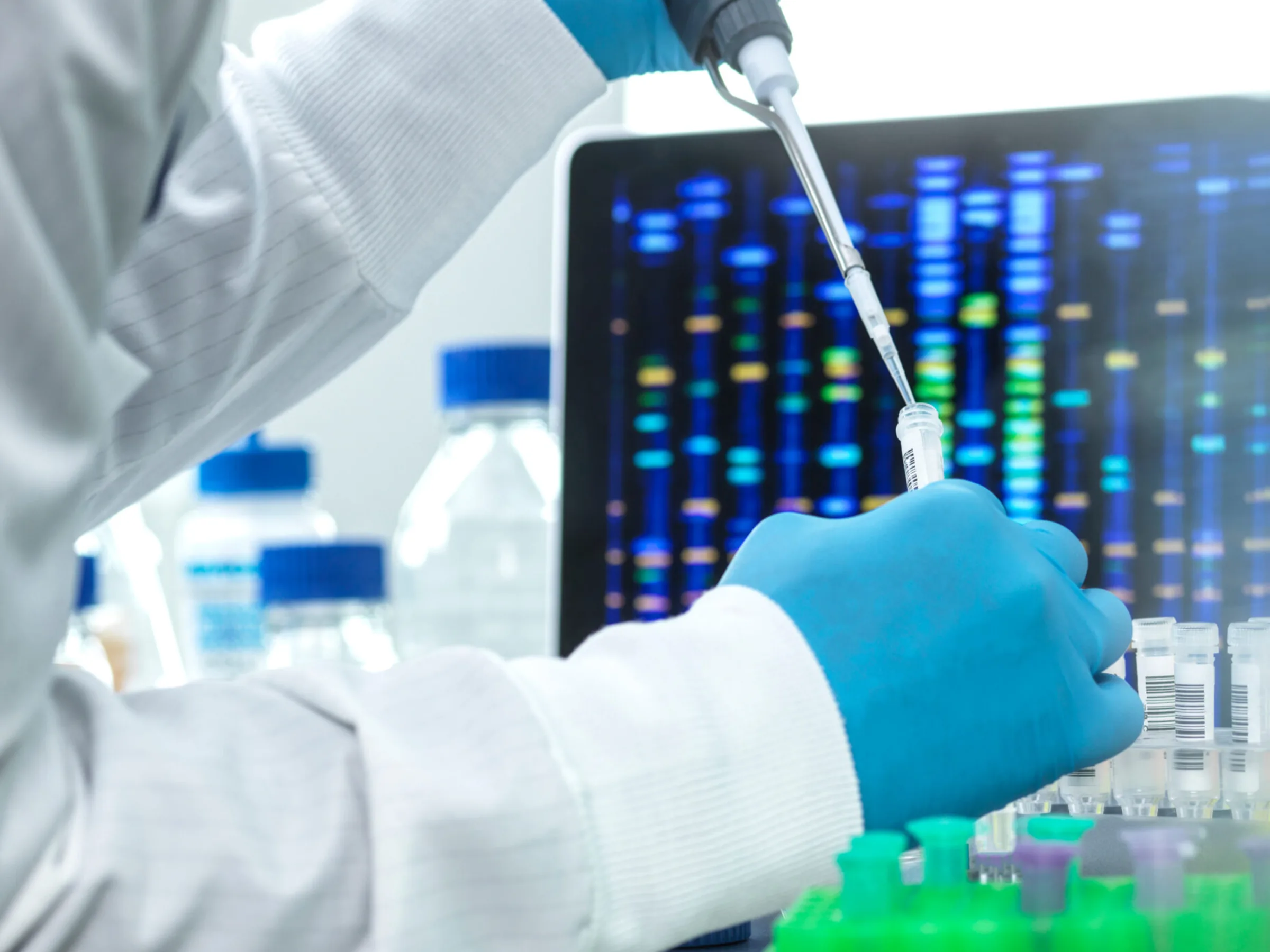 A scientist pipetting samples in front of a sequencing readout