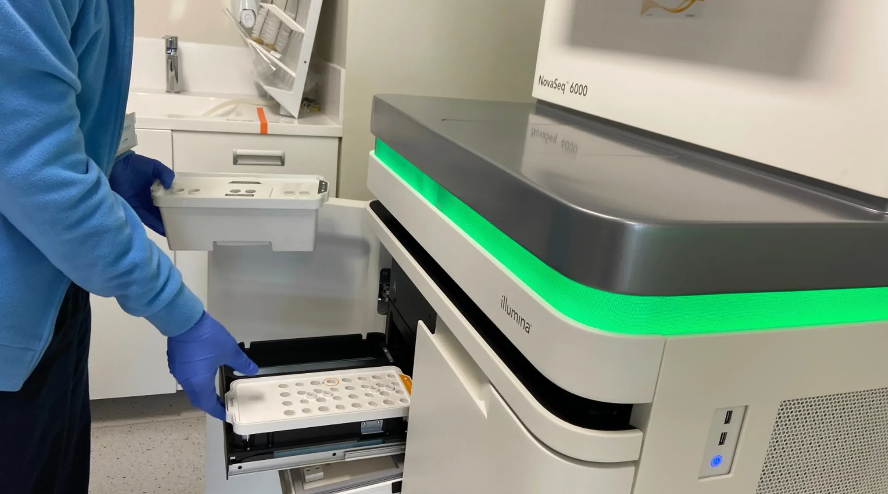 A laboratory scientist loading a sample tray into an Illumina sequencer
